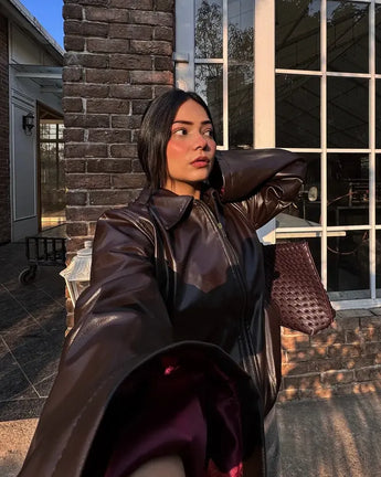 Woman in freyja faux burgundy leather coat standing outside a building with large windows.